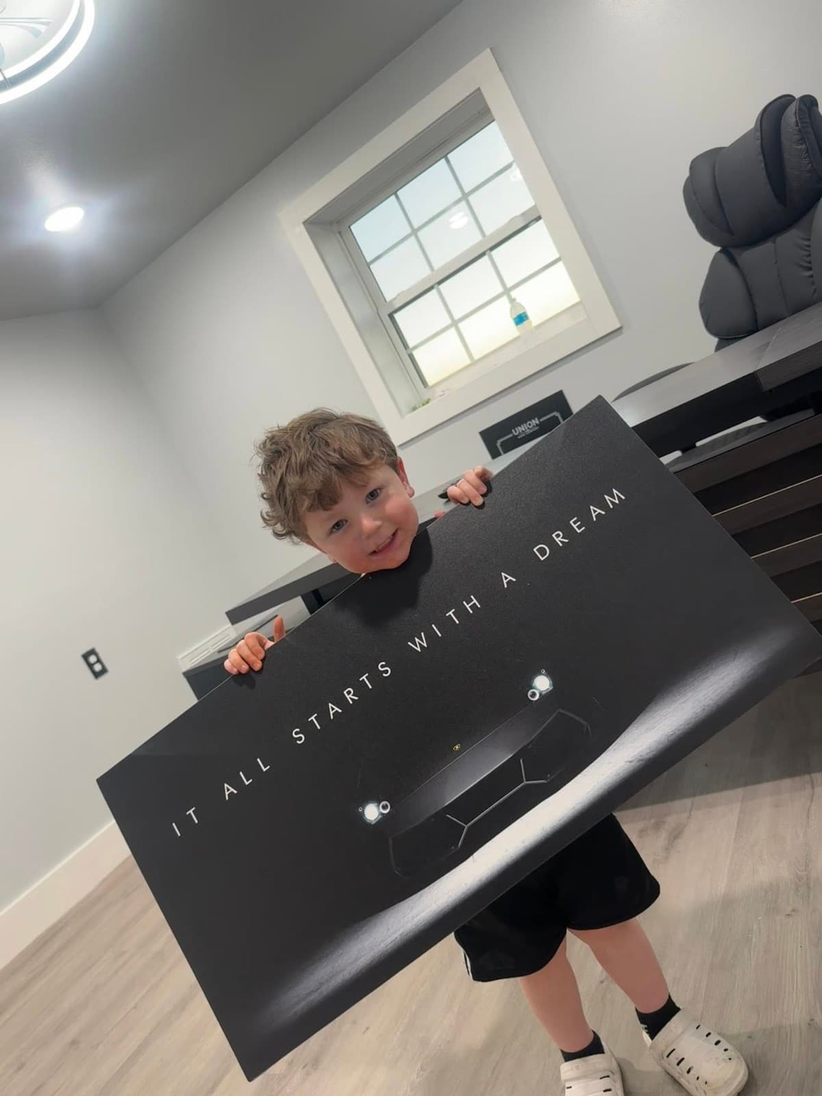 Colin Richard's young son holding an 'It All Starts With A Dream' Lamborghini print at the Elite Custom Automotive shop