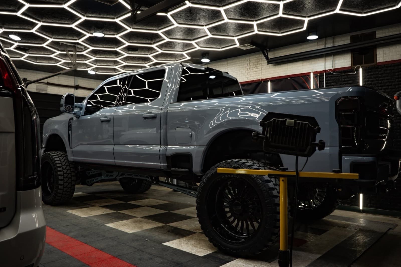 Lifted grey Ford F-250 Super Duty on custom black wheels inside the Elite Custom Automotive hexagon-lit shop in Lockport, LA