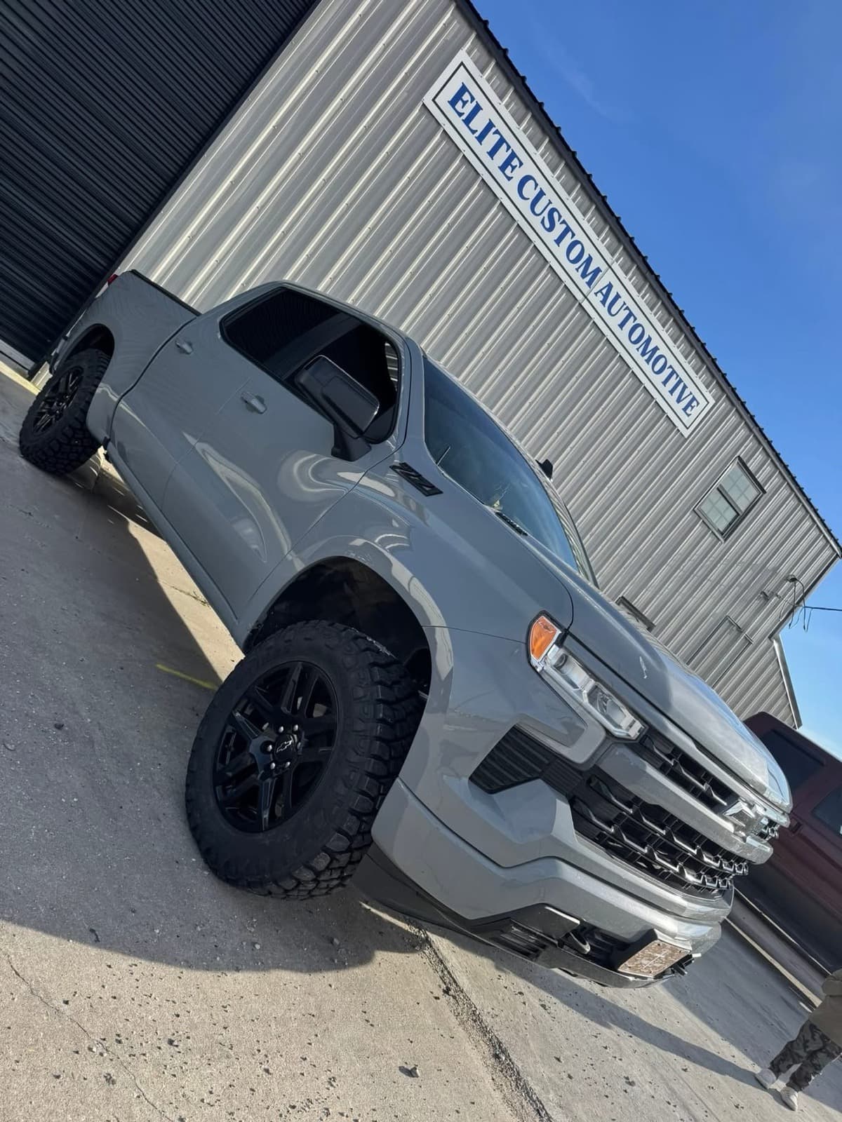 Lifted cement-grey Chevrolet Silverado in front of the Elite Custom Automotive sign in Lockport, LA